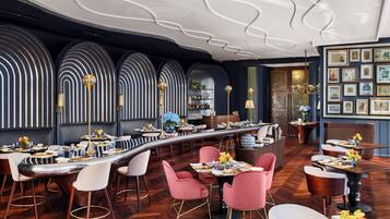 A modern restaurant with a long bar, multiple seating areas, and a decorative ceiling.