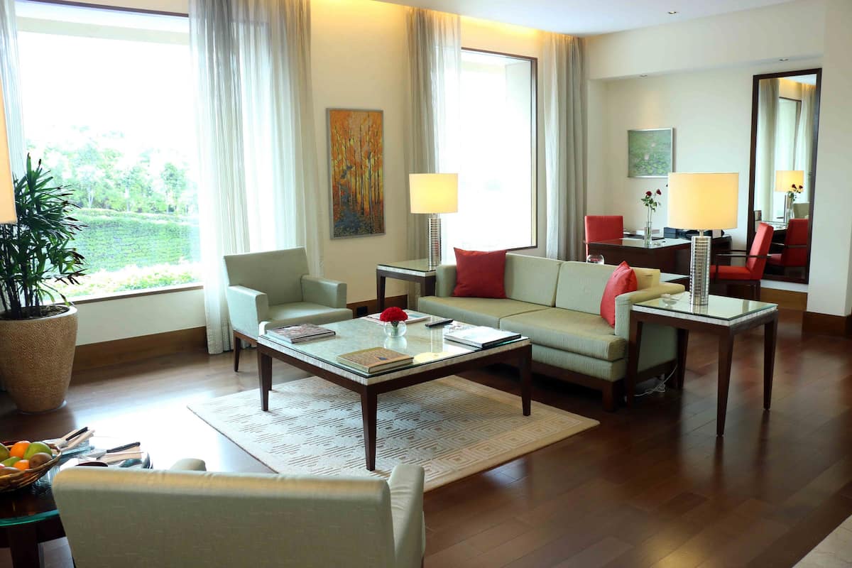 Uma sala de estar moderna com sofá, poltronas, mesa de centro e mesa de jantar. Há uma janela grande com cortinas, uma planta em vaso e obras de arte nas paredes.