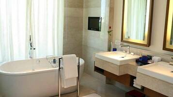 A modern bathroom with a freestanding bathtub, two sinks, a large mirror, and a television mounted on the wall.