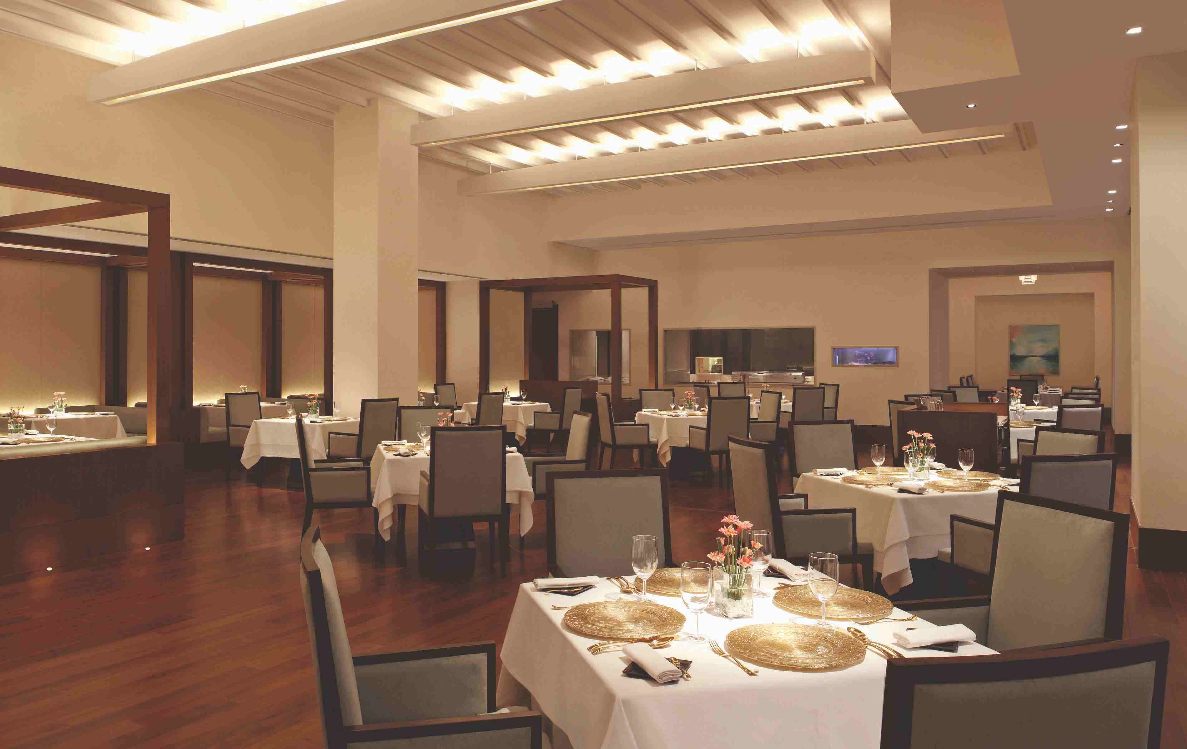 A spacious dining area with multiple tables set for dining, featuring gold-rimmed placemats and white tablecloths.