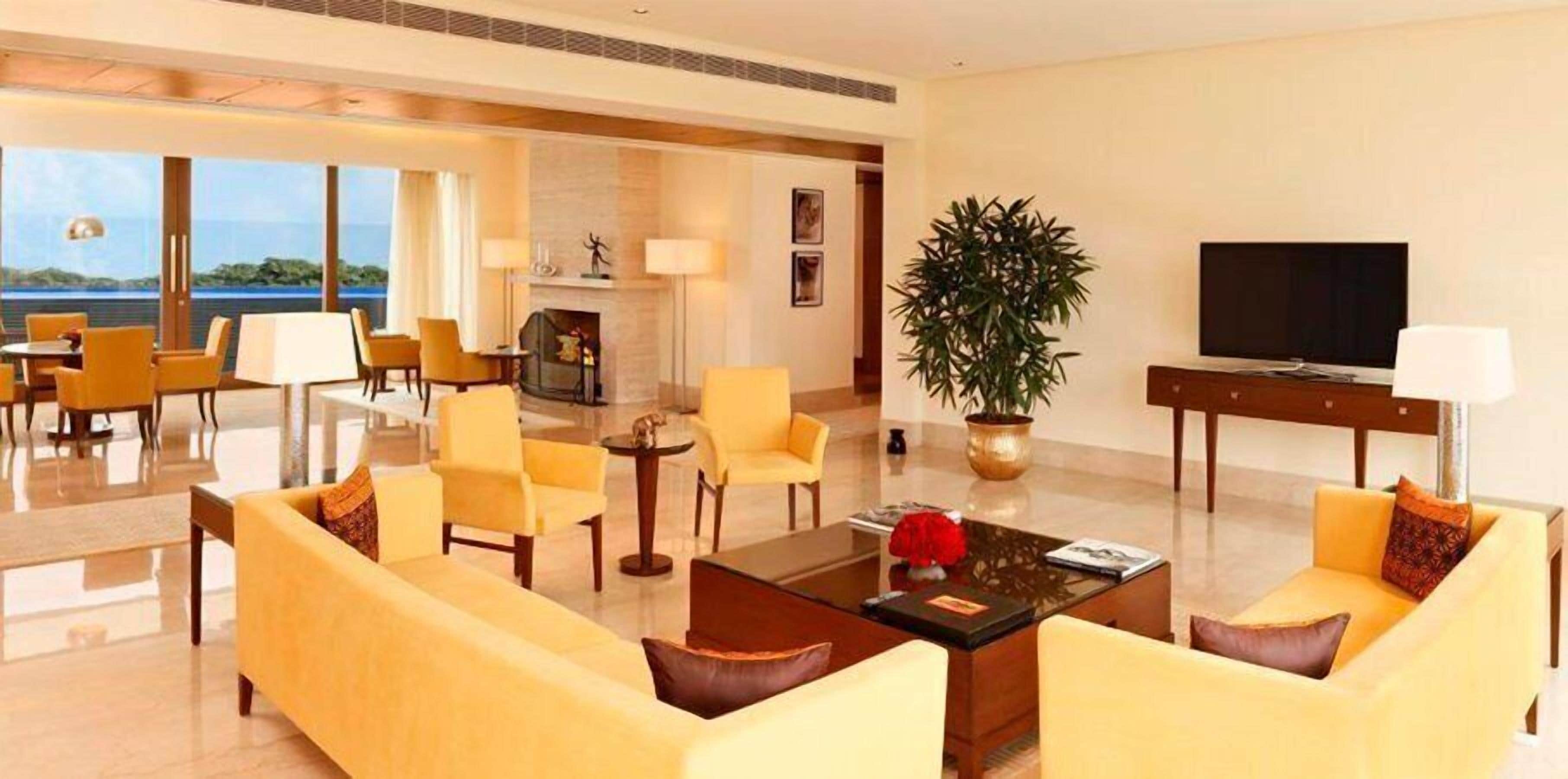 Amplia sala de estar con sofás amarillos, una mesa de centro y un televisor. Hay una planta grande en maceta y una chimenea.