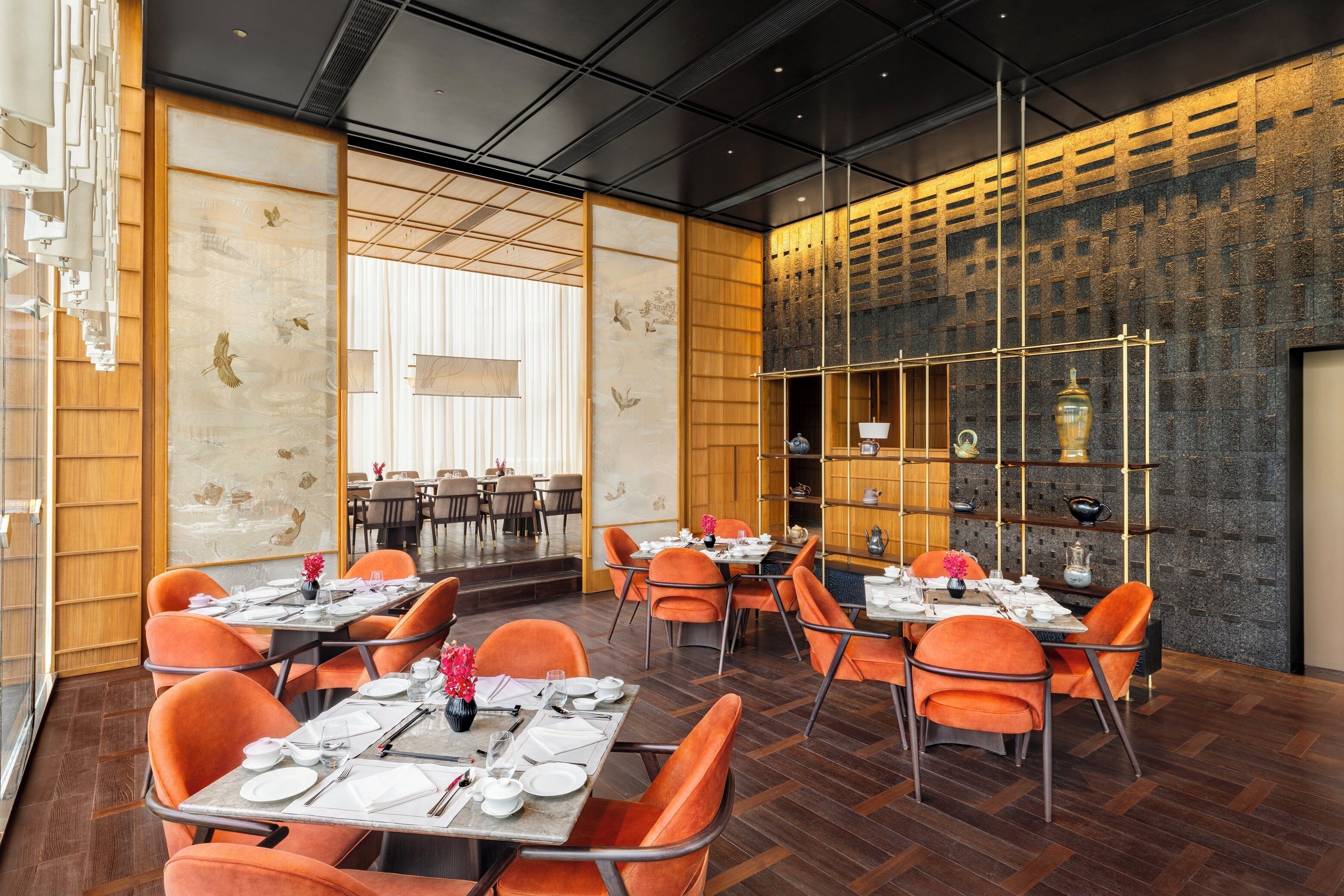 Un ristorante moderno con sedie e tavoli arancioni, pannelli in legno e una parete in mattoni con mensole.