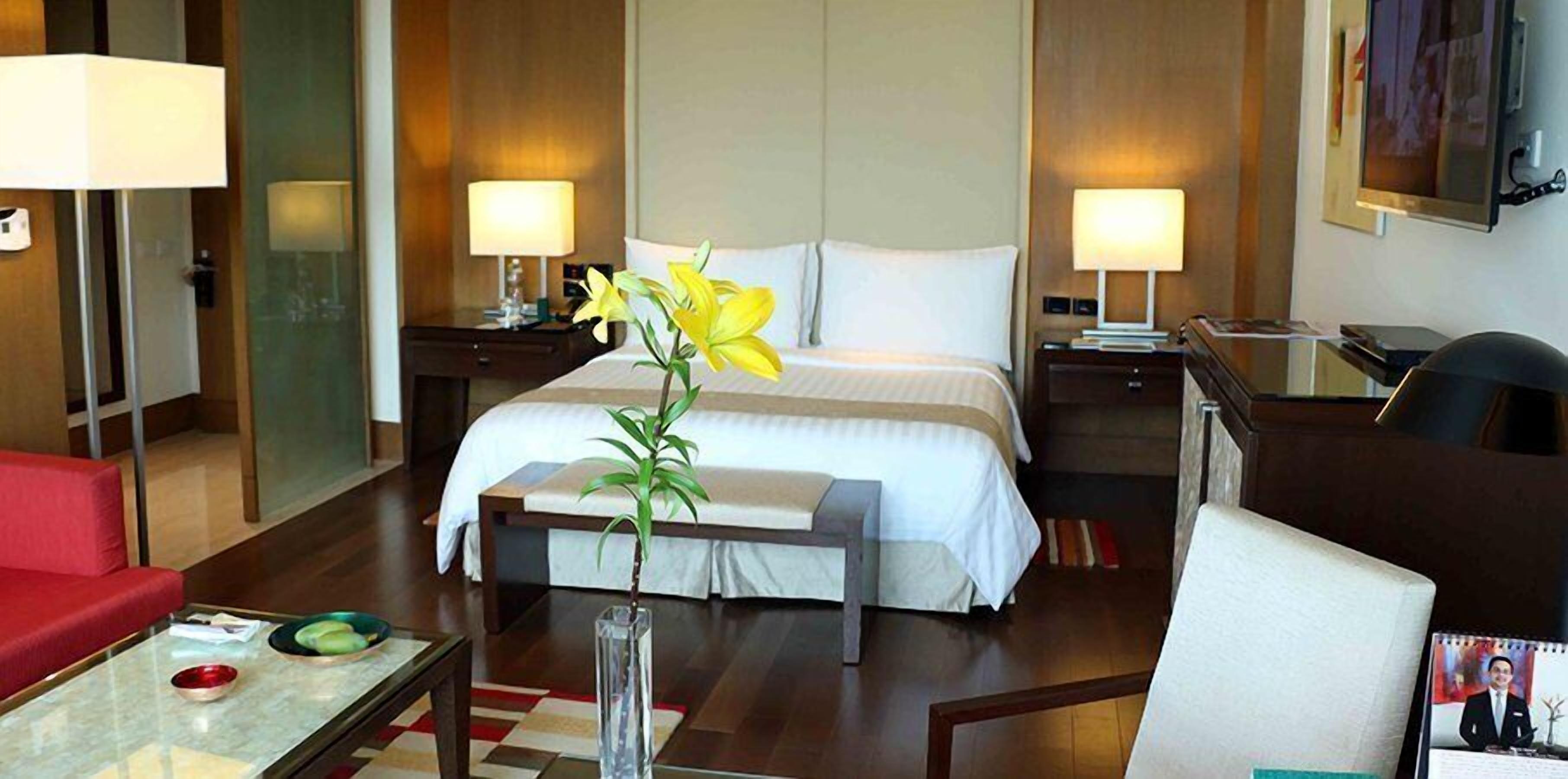 Ein Hotelzimmer mit Bett, Nachttischen, Schreibtisch, Stuhl, Couchtisch und einer Vase mit Blumen.