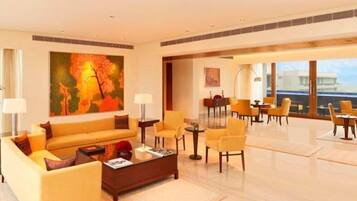 A spacious lobby with a large sofa, armchairs, and a coffee table. There is a painting on the wall and a view of the outside through large windows.