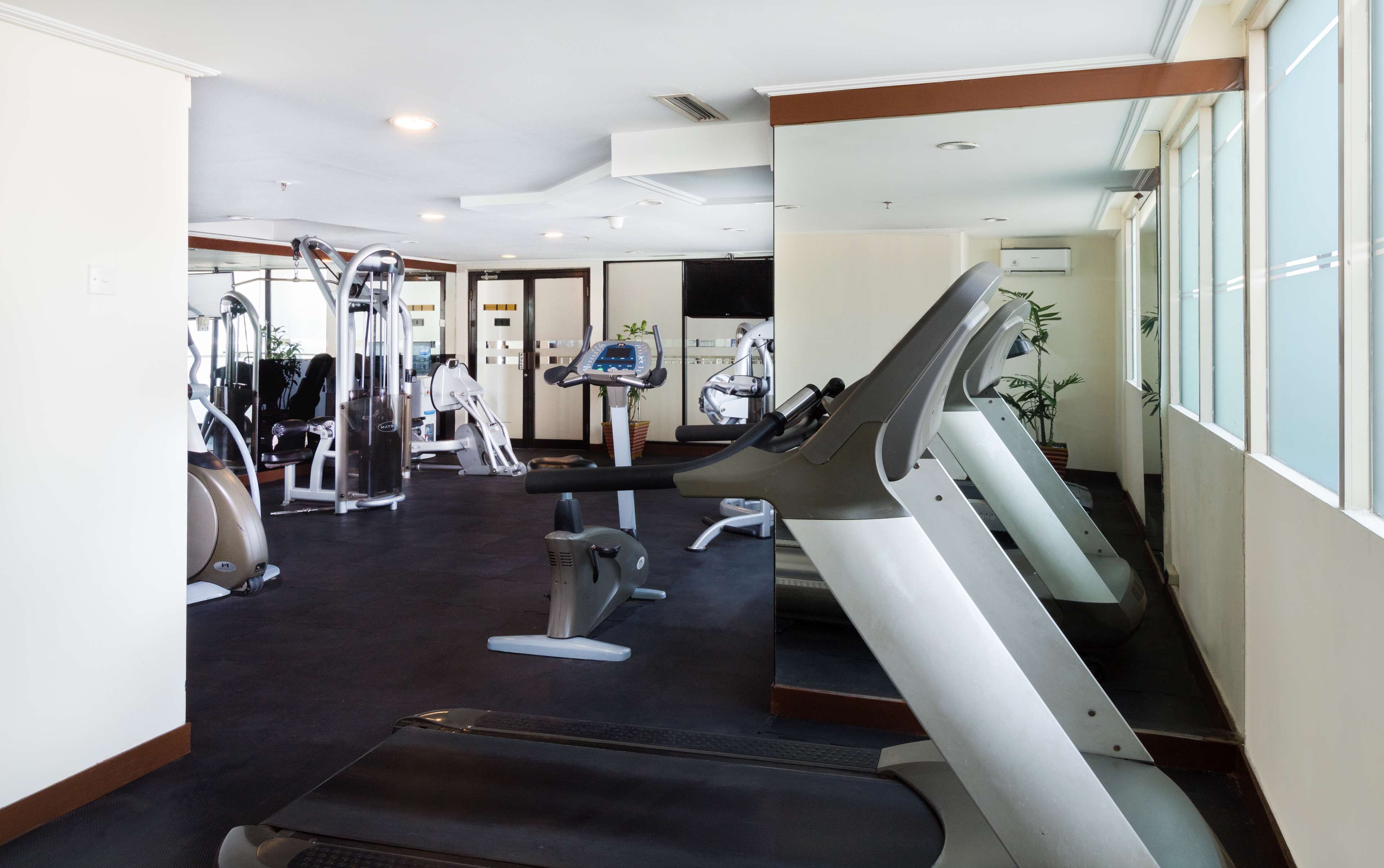 Une salle de sport équipée de tapis de course, d’appareils d’exercice et d’un grand miroir.