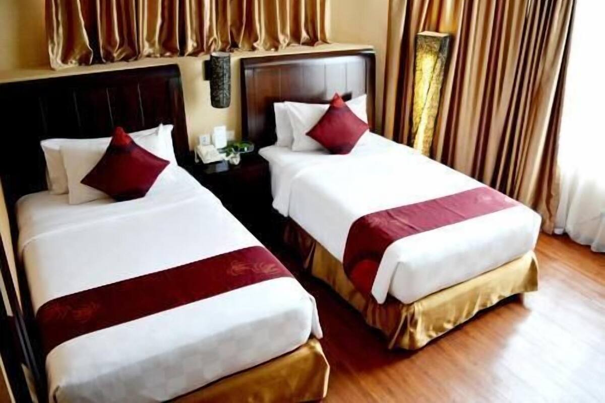 Two adjacent hotel beds with headboards, a nightstand, and a mirror between them.