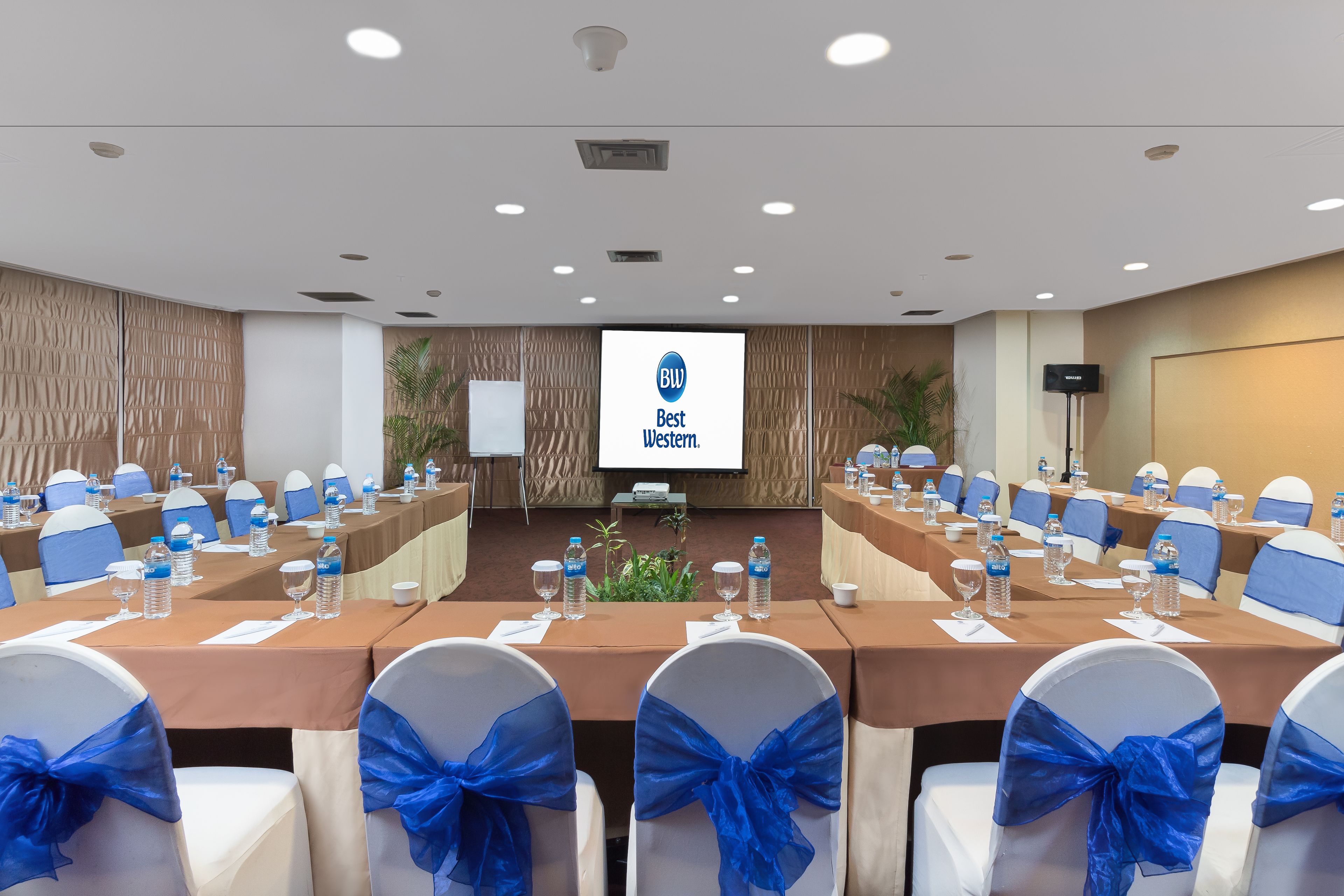 Un salón de conferencias con una mesa larga, sillas azules y blancas y una pantalla que muestra 