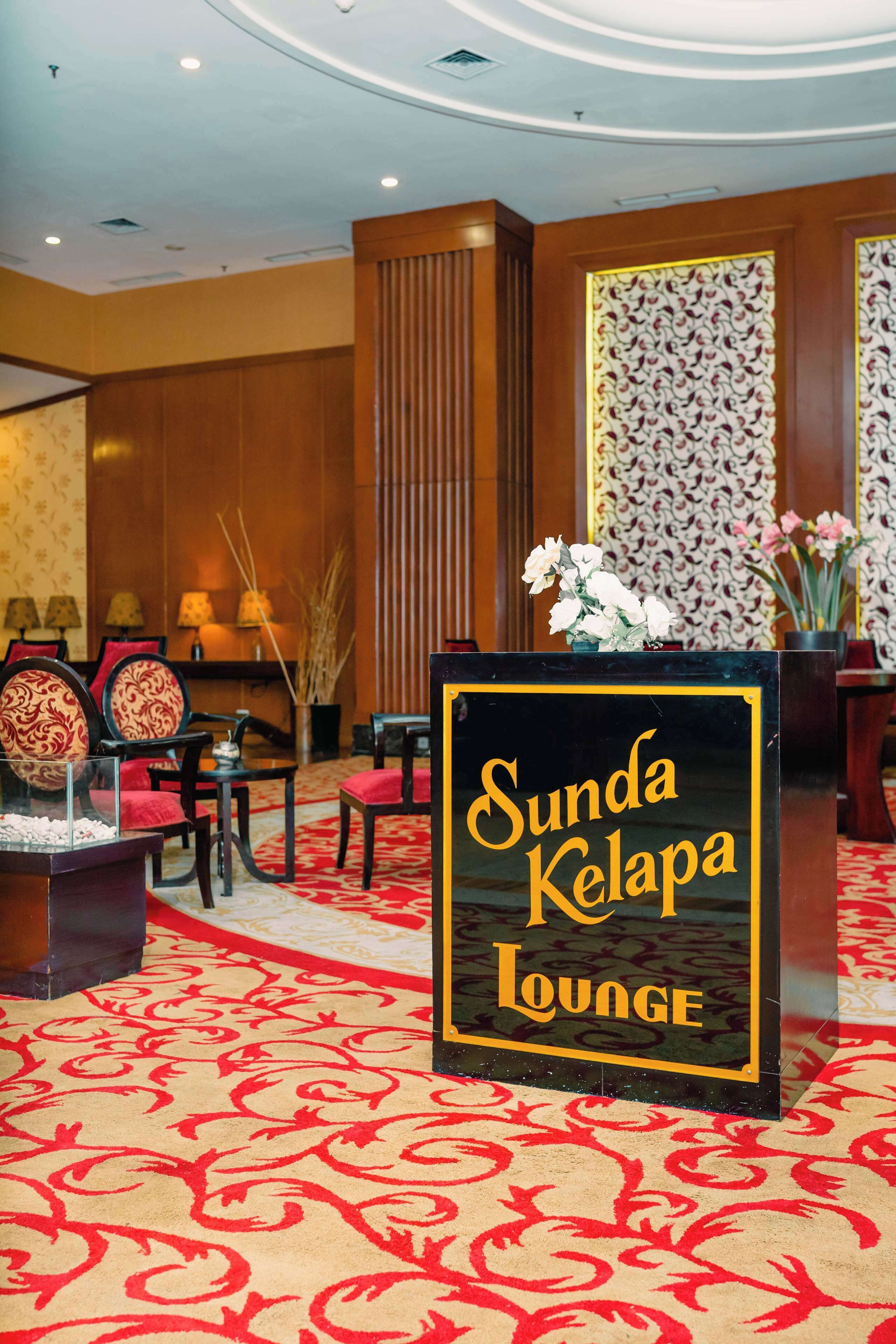 Eine Lobby mit rotem Teppich, einem Empfangstresen mit der Aufschrift 'Sunda Kelapa Lounge' und traditioneller Einrichtung, darunter Holzwände und gestaltete Tapeten.