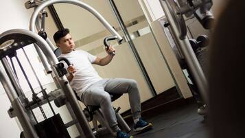 Um homem usando um aparelho de leg press numa academia com paredes espelhadas e uma pilha de pesos visível.
