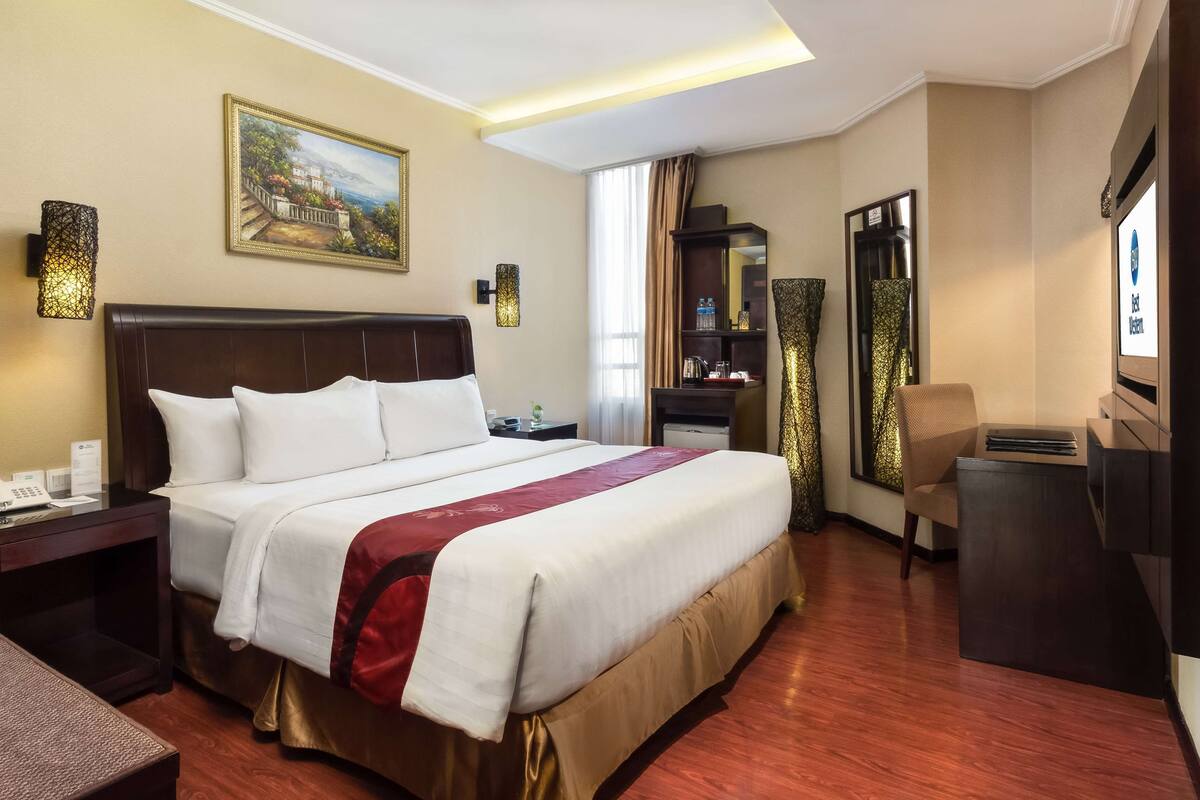 A hotel room with a large bed, a desk, a chair, a TV, and a painting on the wall.