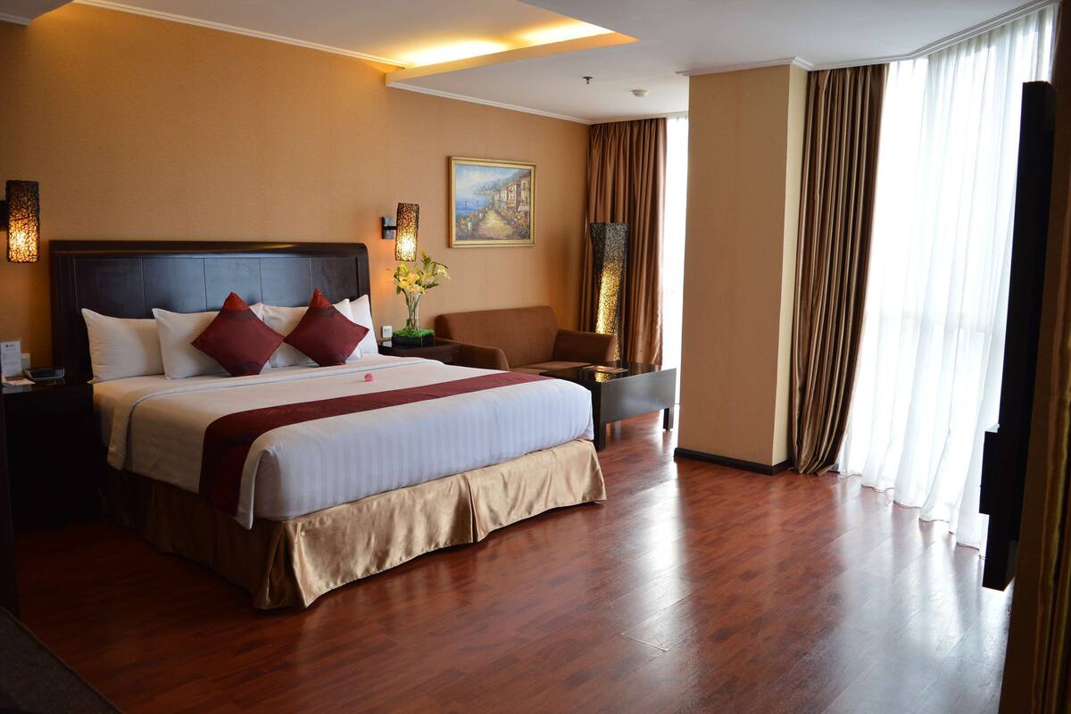 A hotel room with a large bed, a nightstand, a chair, a desk, and a window with curtains.