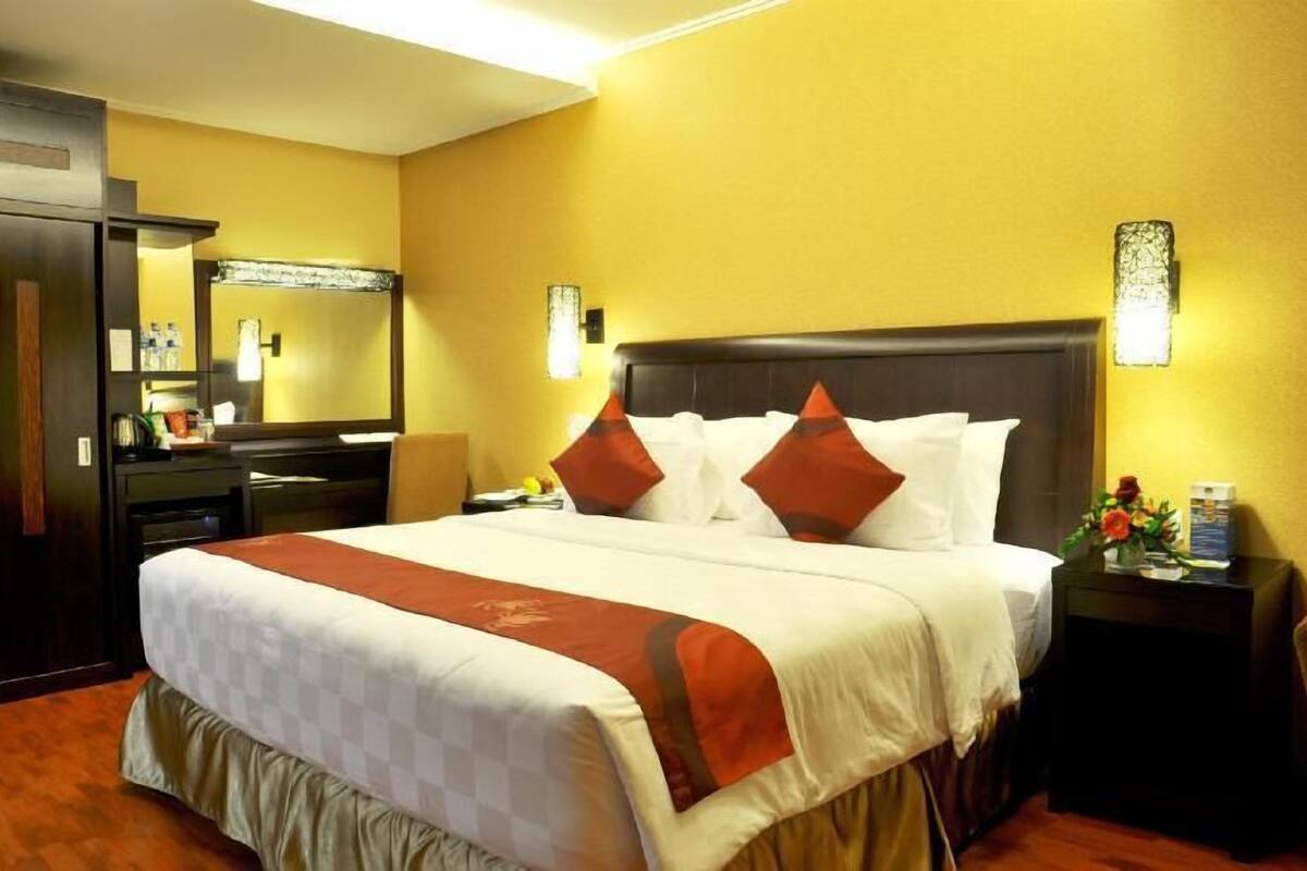 A hotel room with a large bed, a nightstand, a dresser, a mirror, and a wall-mounted light fixture.