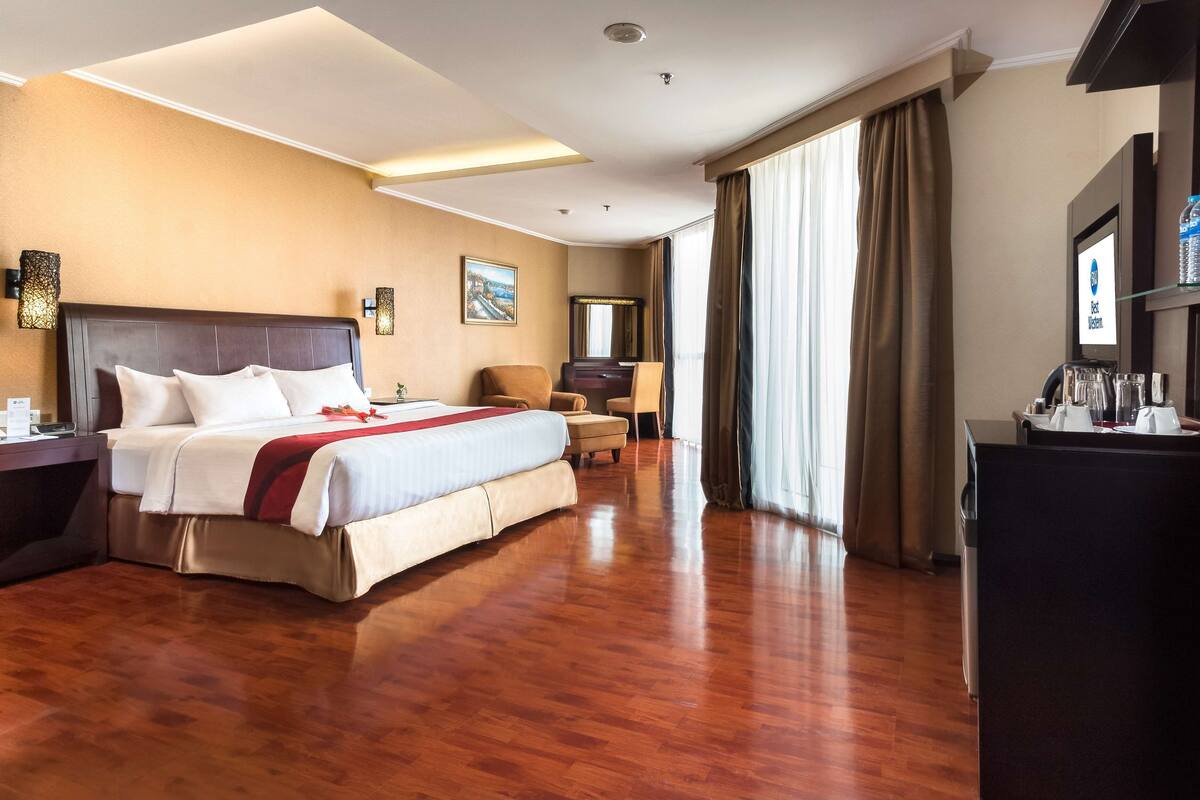 A hotel room with a large bed, a desk, a chair, and a television.
