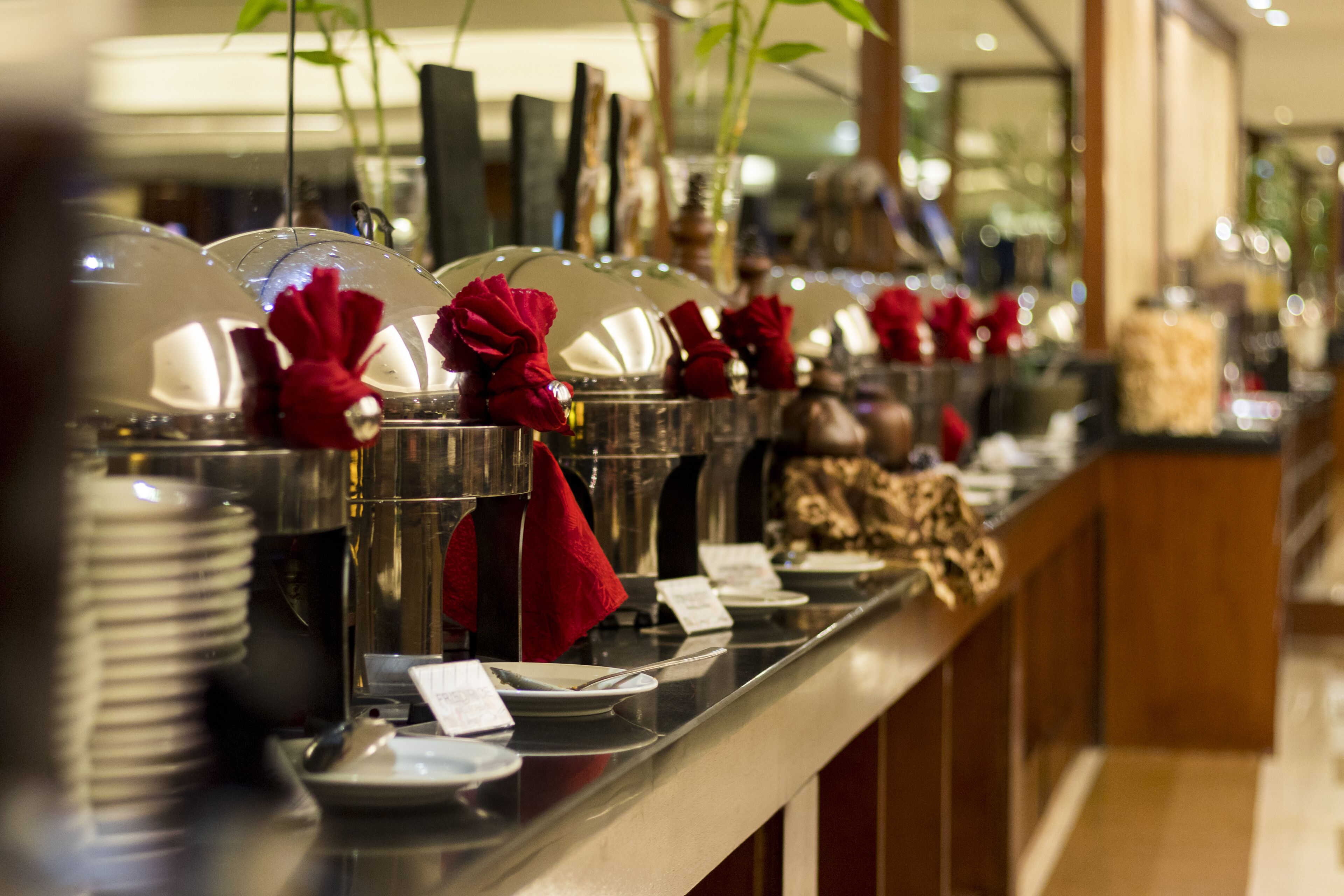 A buffet line with multiple food stations, each with a glass dome cover and a red napkin.