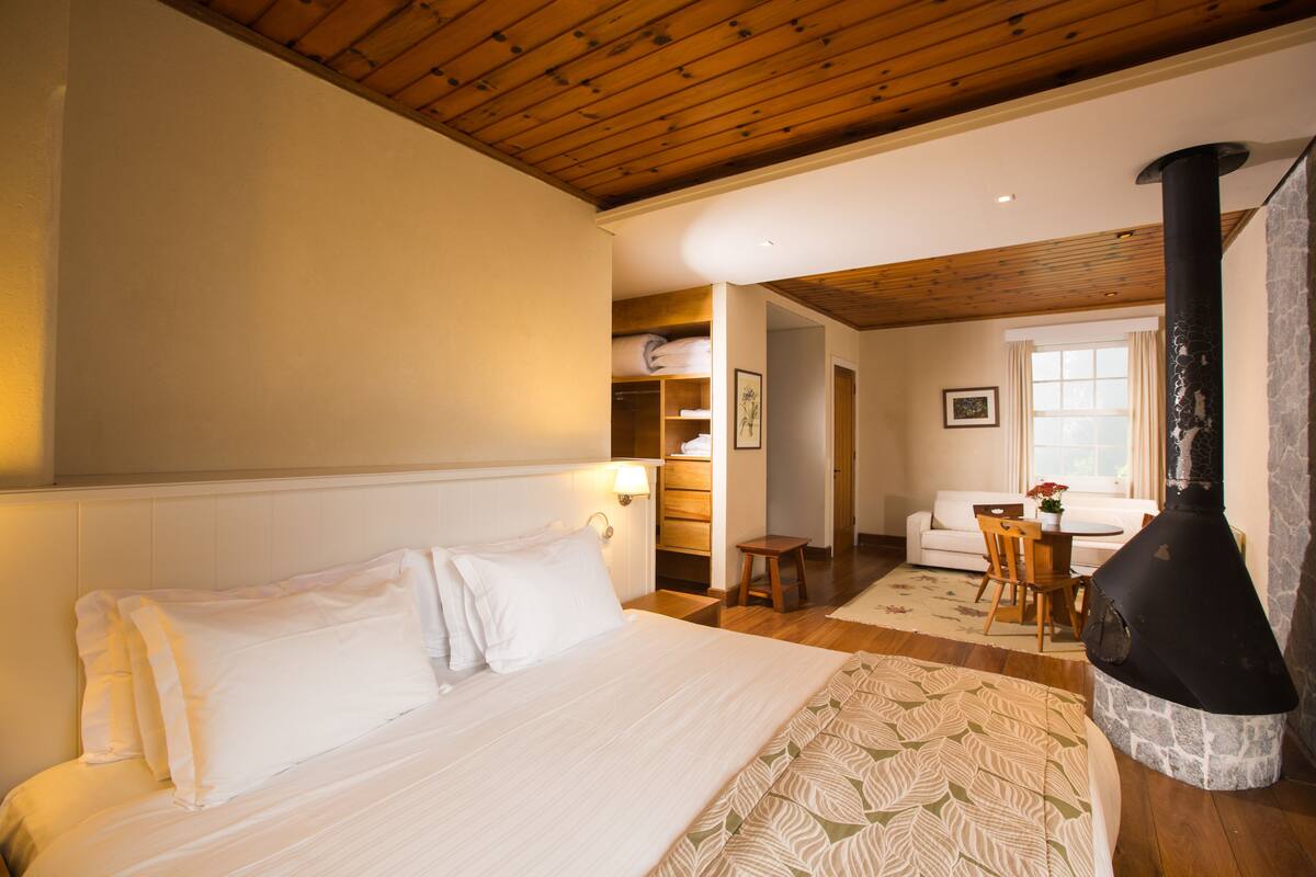 Une chambre à coucher comprenant un lit, un plafond en bois, une cheminée en pierre, un canapé et une table à manger avec des chaises.