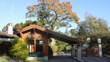 A lodge with a covered entrance, a prominent tree with red flowers, and a clear sky.