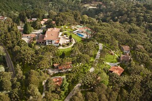 An aerial view of a residential area with multiple houses, a swimming pool, and a tennis court surrounded by dense greenery. - Hotel Toriba (Campos do Jordão)
