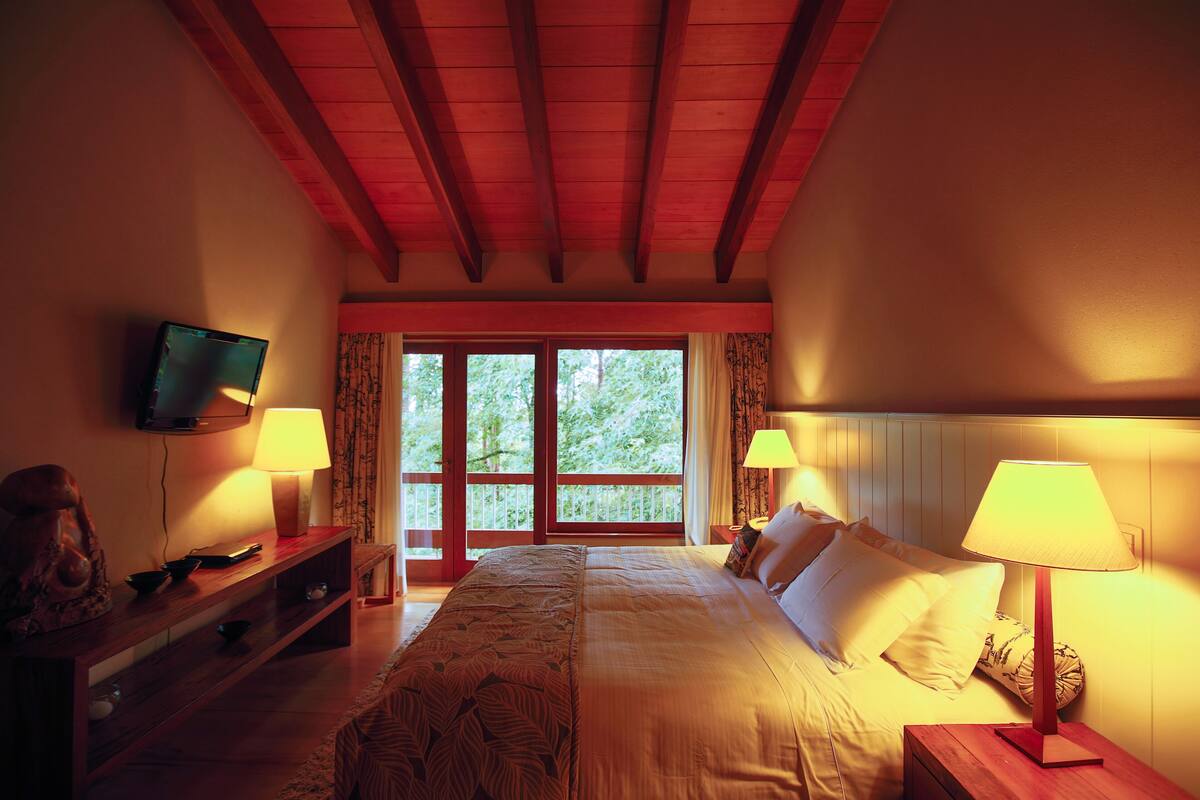 Une chambre à coucher avec un grand lit, deux lampes de chevet, un téléviseur fixé au mur et un banc en bois.