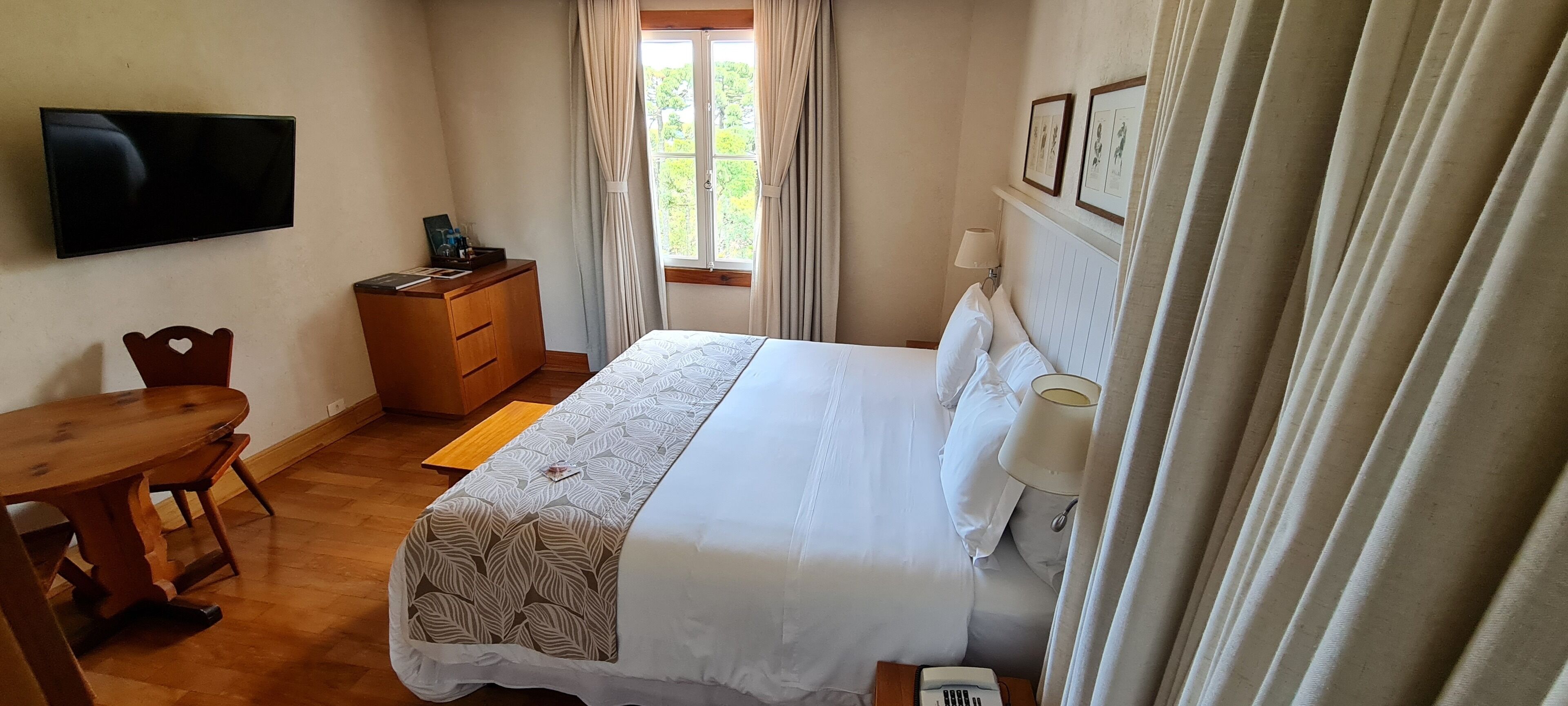 A hotel room with a bed, bedside table, wooden desk, and a television on the wall.