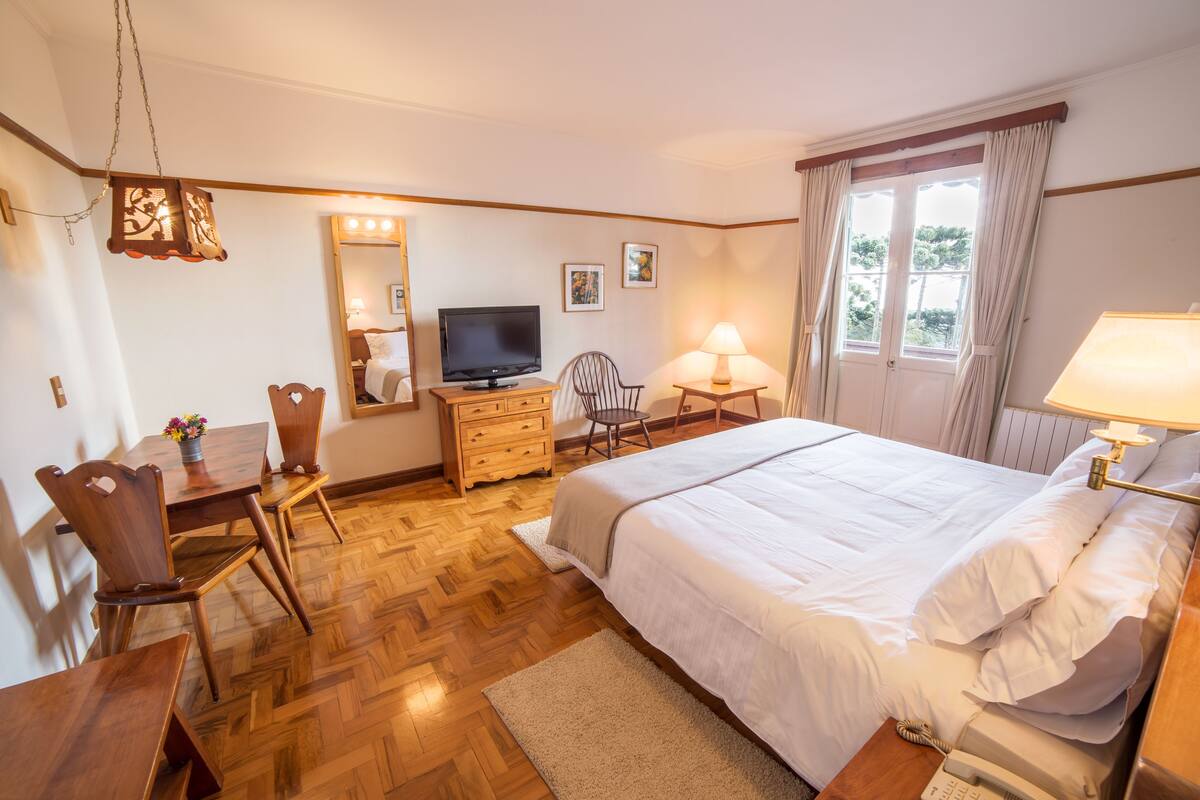 Une chambre d’hôtel équipée d’un lit, d’un bureau, d’une chaise, d’une télévision et d’une fenêtre avec des rideaux.