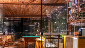 Una zona de bar con mesa de billar, taburetes y estantes llenos de botellas y vasos.