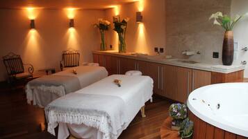Un cuarto de spa con dos camillas, una bañera grande y piso de madera.