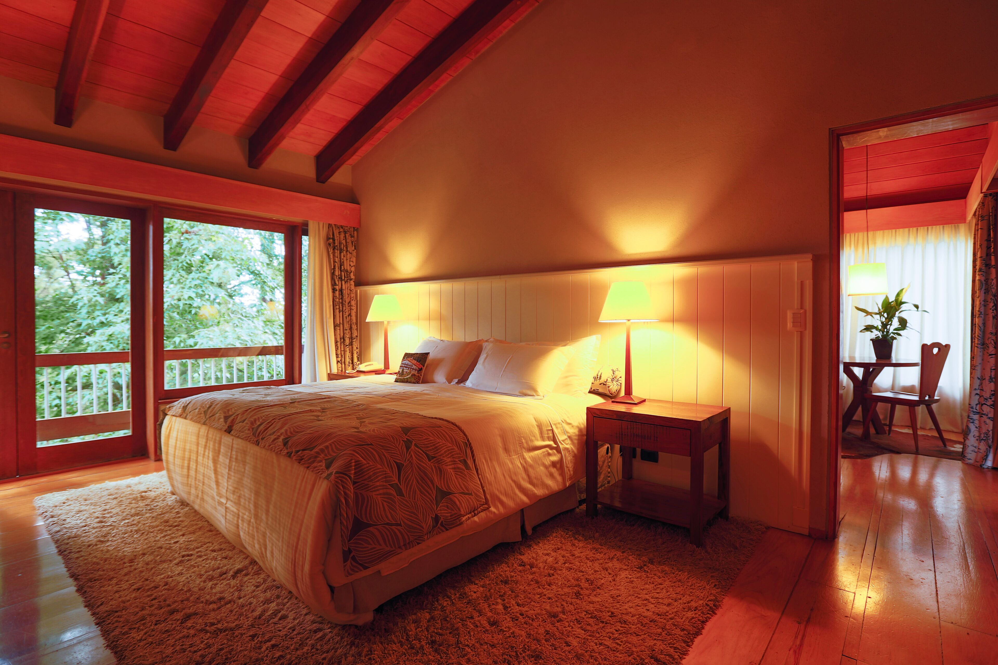 A bedroom with a large bed, two bedside lamps, a wooden nightstand, and a view of the outdoors through a sliding door.