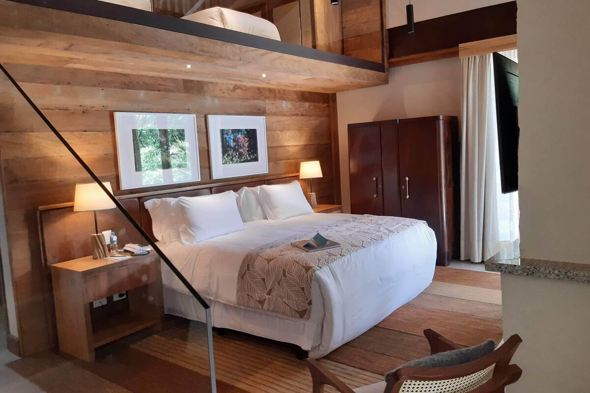 Une chambre d’hôtel comprenant un lit, des tables de chevet, une chaise, une armoire et des tableaux encadrés accrochés au mur.