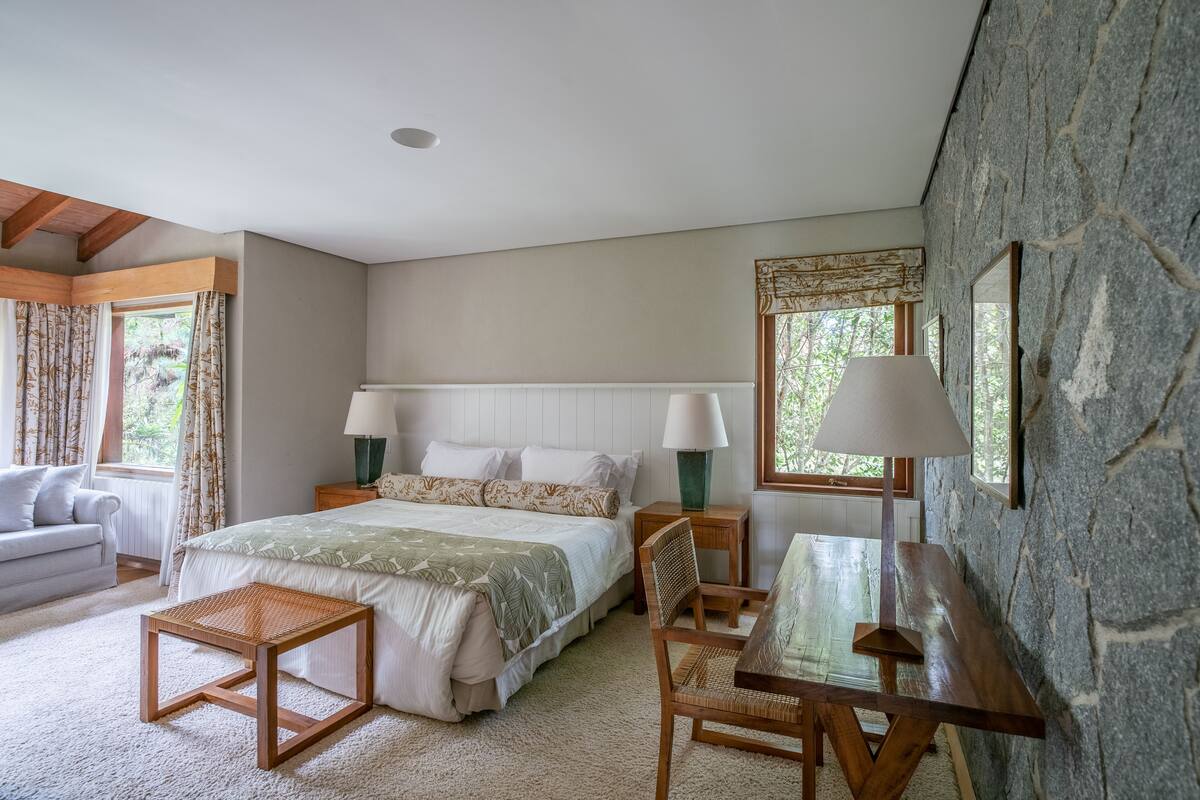 Une chambre à coucher comprenant un lit, des tables de chevet, une chaise, une petite table et une fenêtre avec des rideaux.