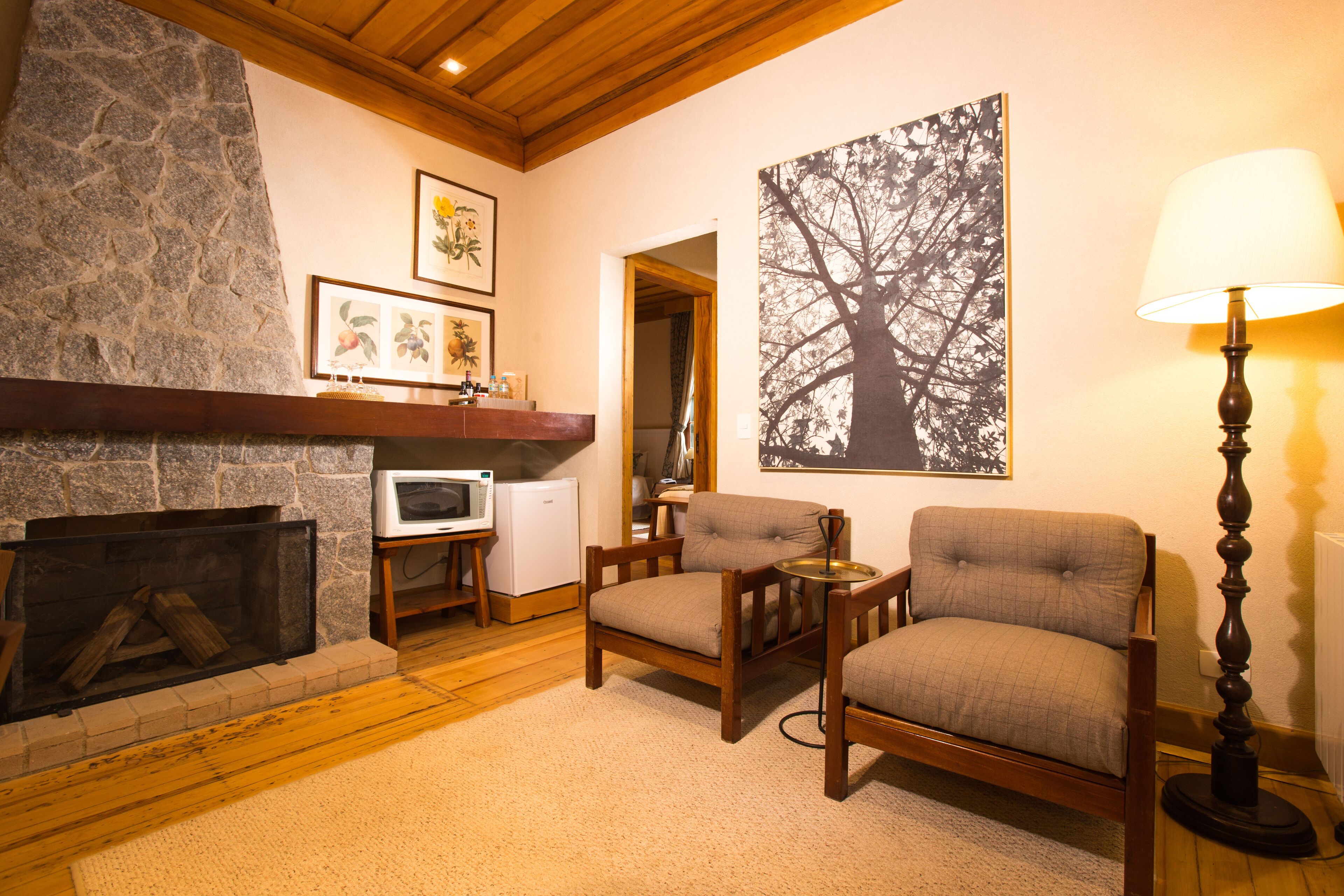 A cozy living room with a stone fireplace, wooden furniture, a large framed tree artwork, and a floor lamp.