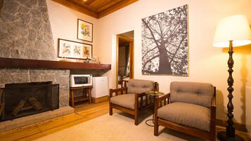 A cozy living room with a stone fireplace, wooden furniture, a large framed tree artwork, and a floor lamp.
