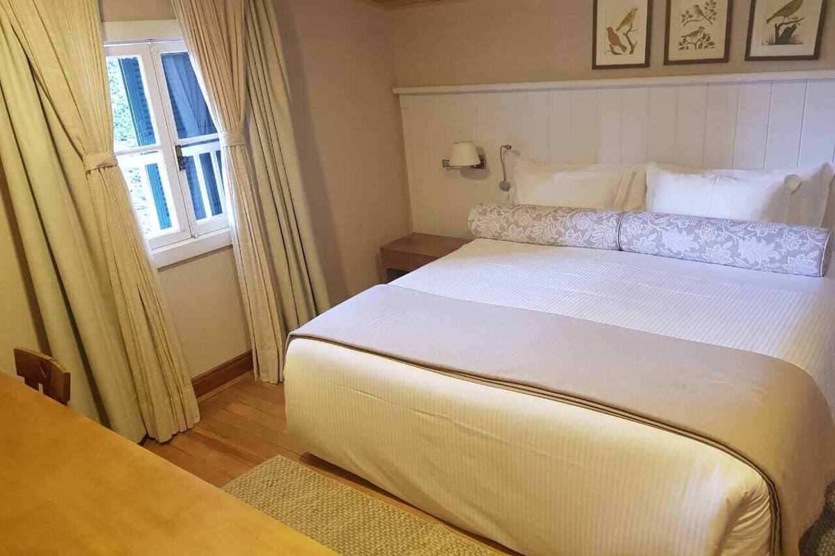 Une chambre à coucher avec un grand lit, une table de chevet, une commode et une fenêtre avec des rideaux.