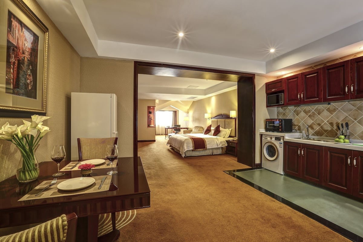 A hotel room with a dining area, a bed, a kitchen, and a bathroom.