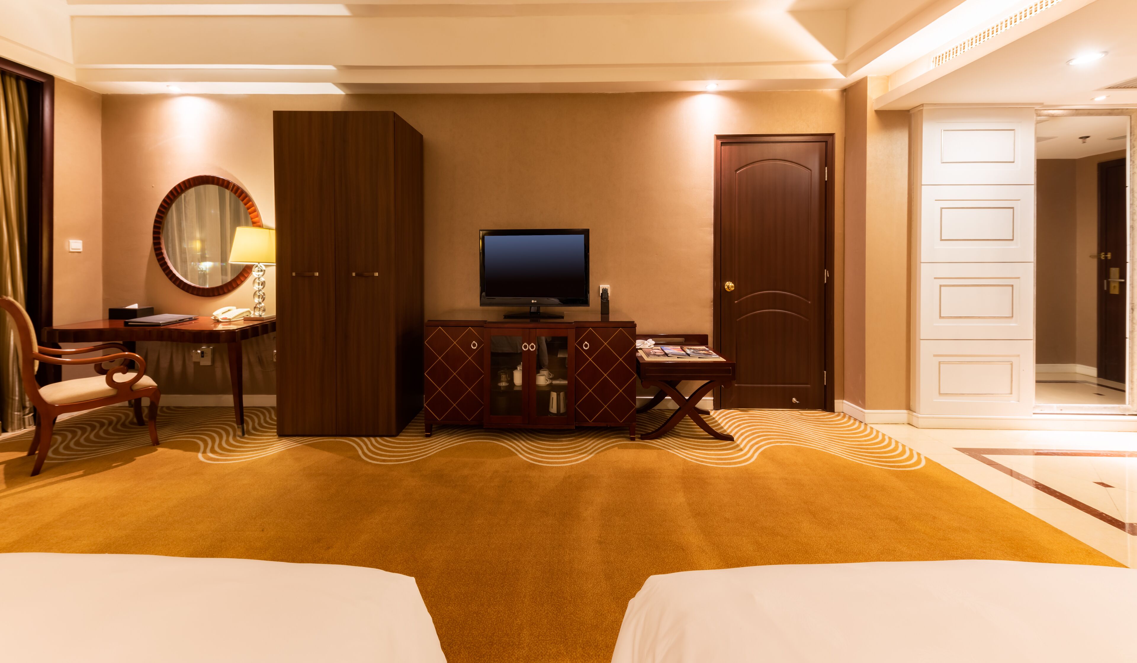 Quarto de hotel com uma cama, escrivaninha, televisão e guarda-roupa.