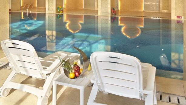 A poolside area with two white lounge chairs, a table with fruits and a drink, and a reflection of the pool. - Country Garden Phoenix Hotels Shenyang Yuhong (Shenyang)