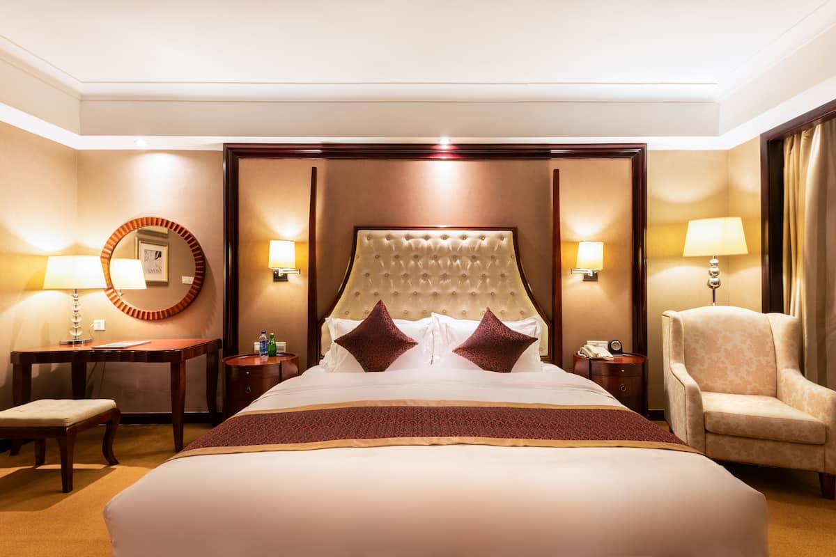A hotel room with a large bed, two bedside tables, a chair, and a mirror.