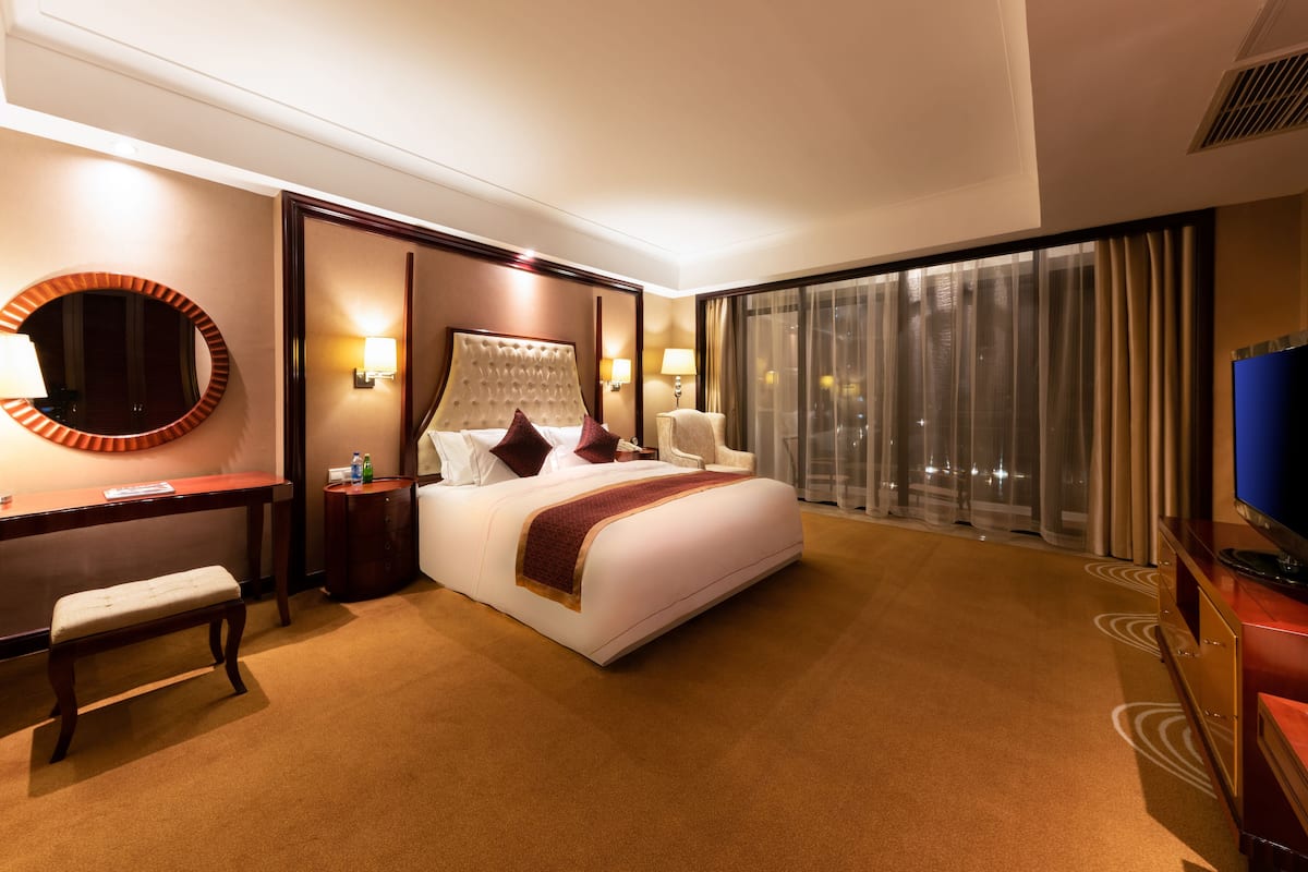 A hotel room with a bed, bedside table, lamp, chair, and a television.