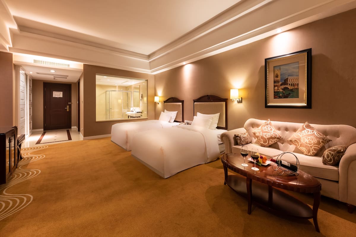 A hotel room with a large bed, a sofa, a coffee table, and a painting on the wall.