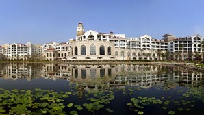 Un hotel con un lago amplio y reflectante al frente, destacando un edificio con torre y ventanas de arco.