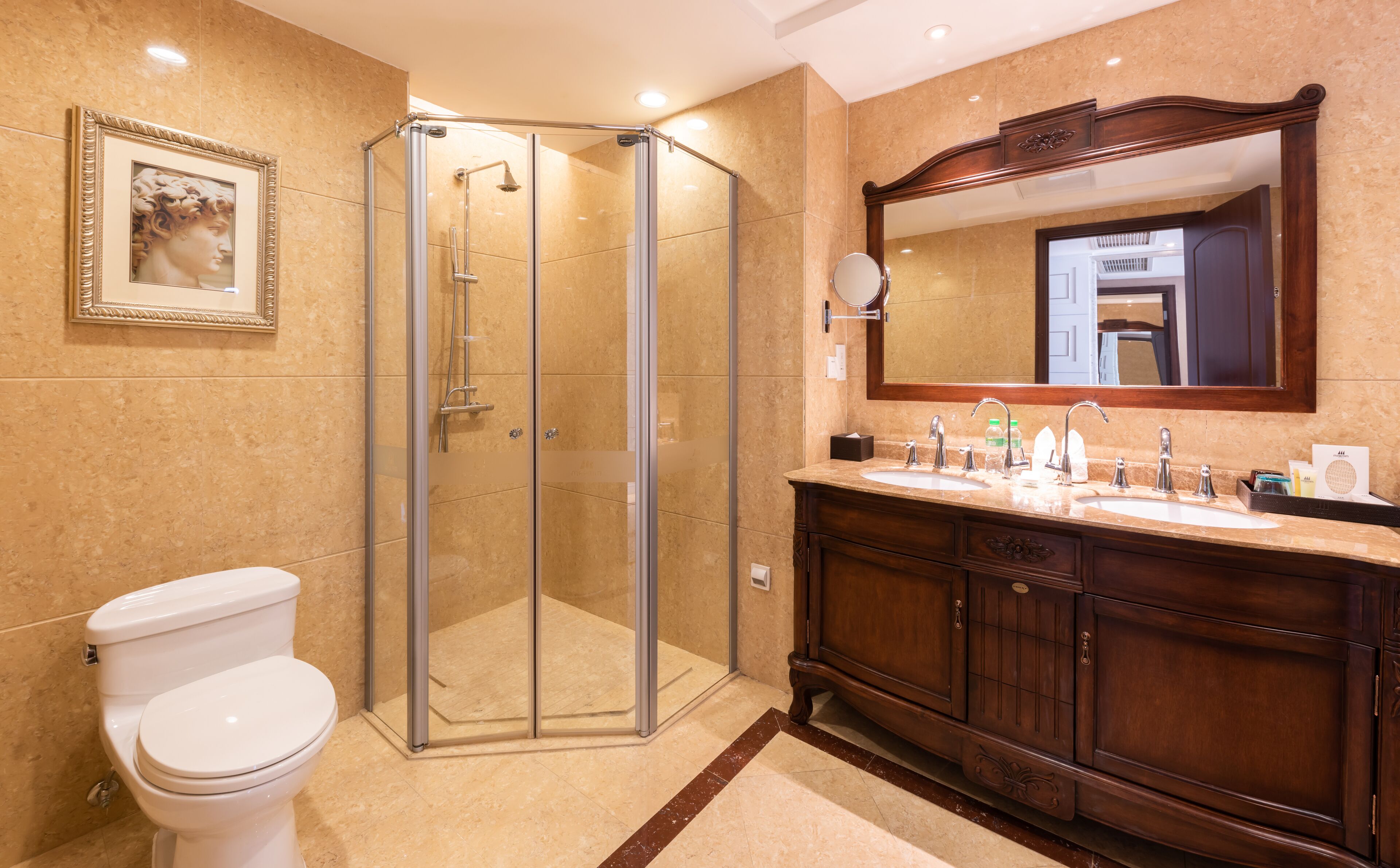 A bathroom with a glass-enclosed shower, a white toilet, a wooden vanity with two sinks, and a large mirror above the vanity.