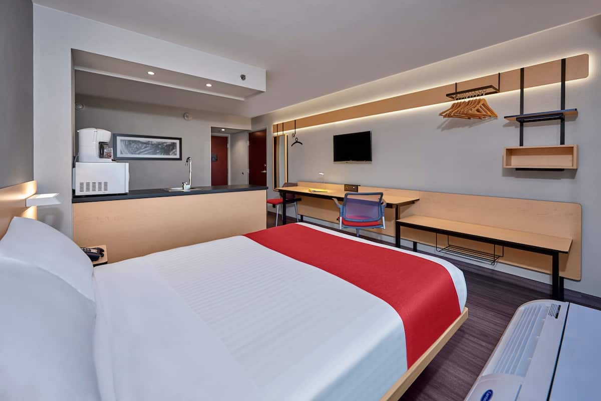 A hotel room with a large bed, a desk with a chair, a television, and a coffee machine.