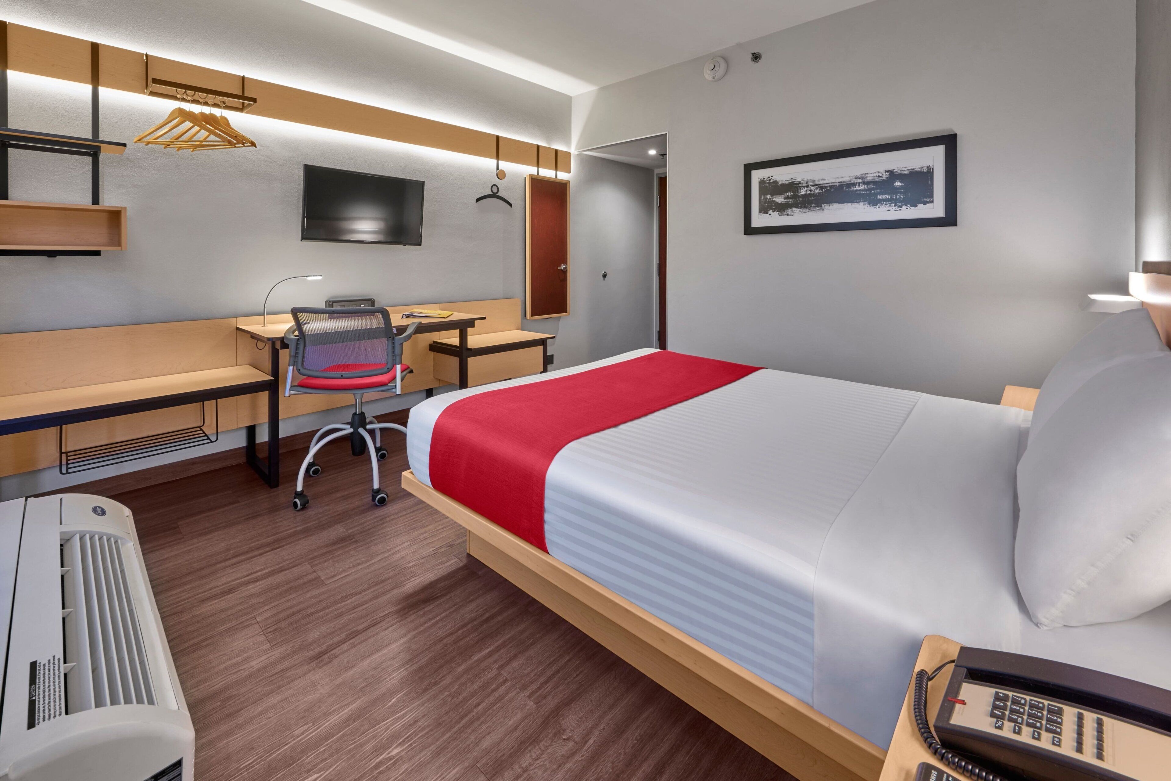A hotel room with a bed, desk, chair, and a heater.