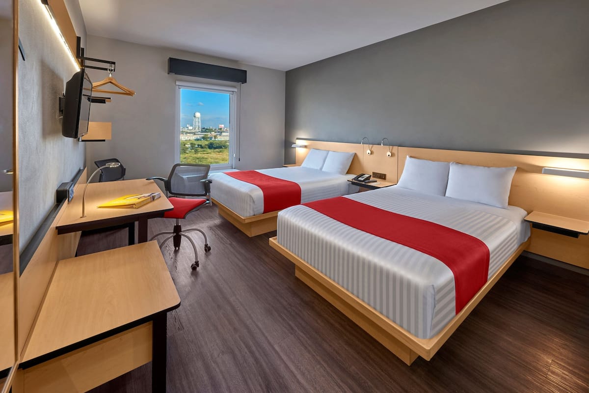 A hotel room with two beds, a desk, a chair, a TV, and a window with a city view.