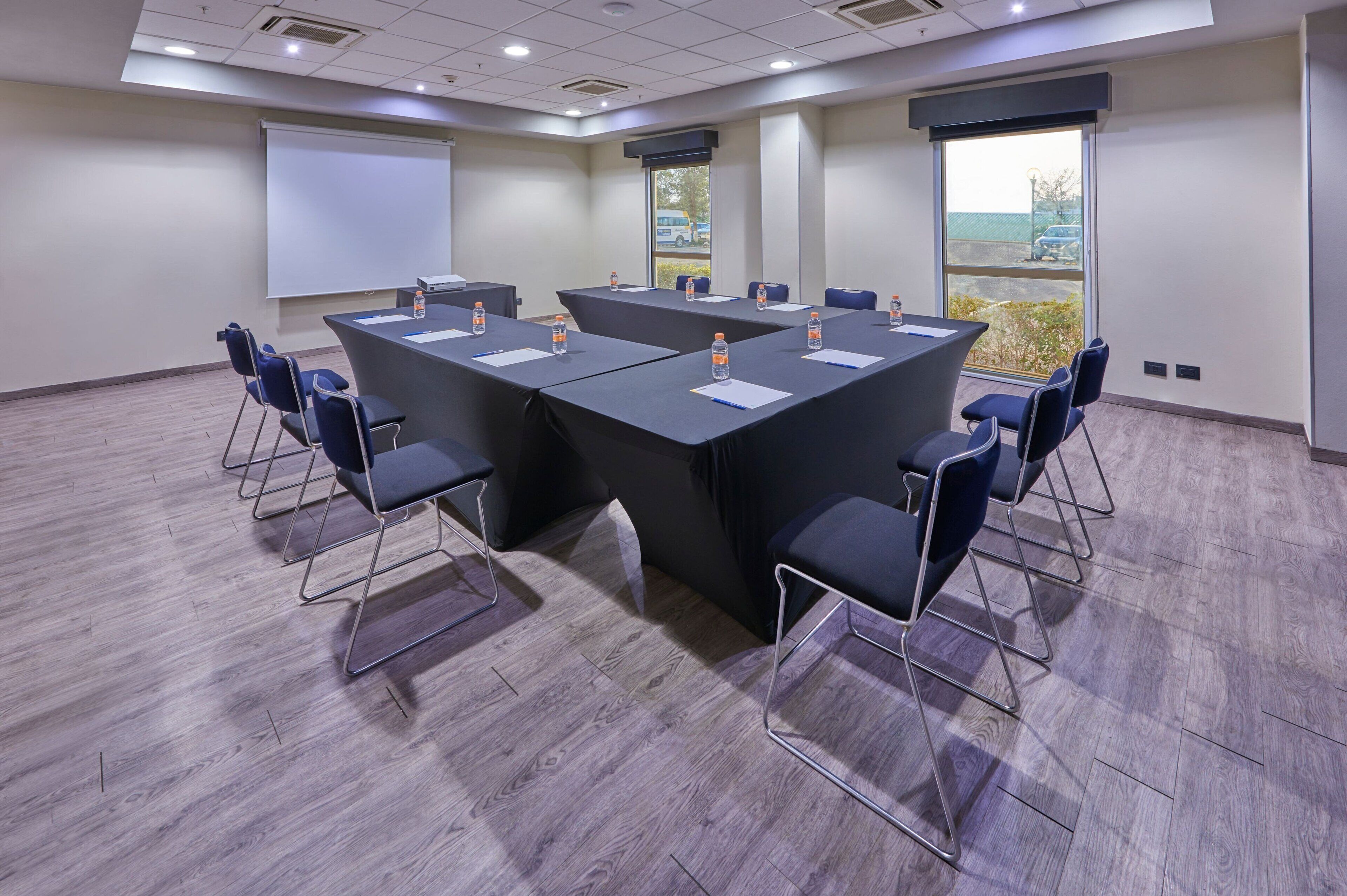 Ein Konferenzraum mit einem großen Tisch, Stühlen, einer Projektionsleinwand und Blick ins Freie.