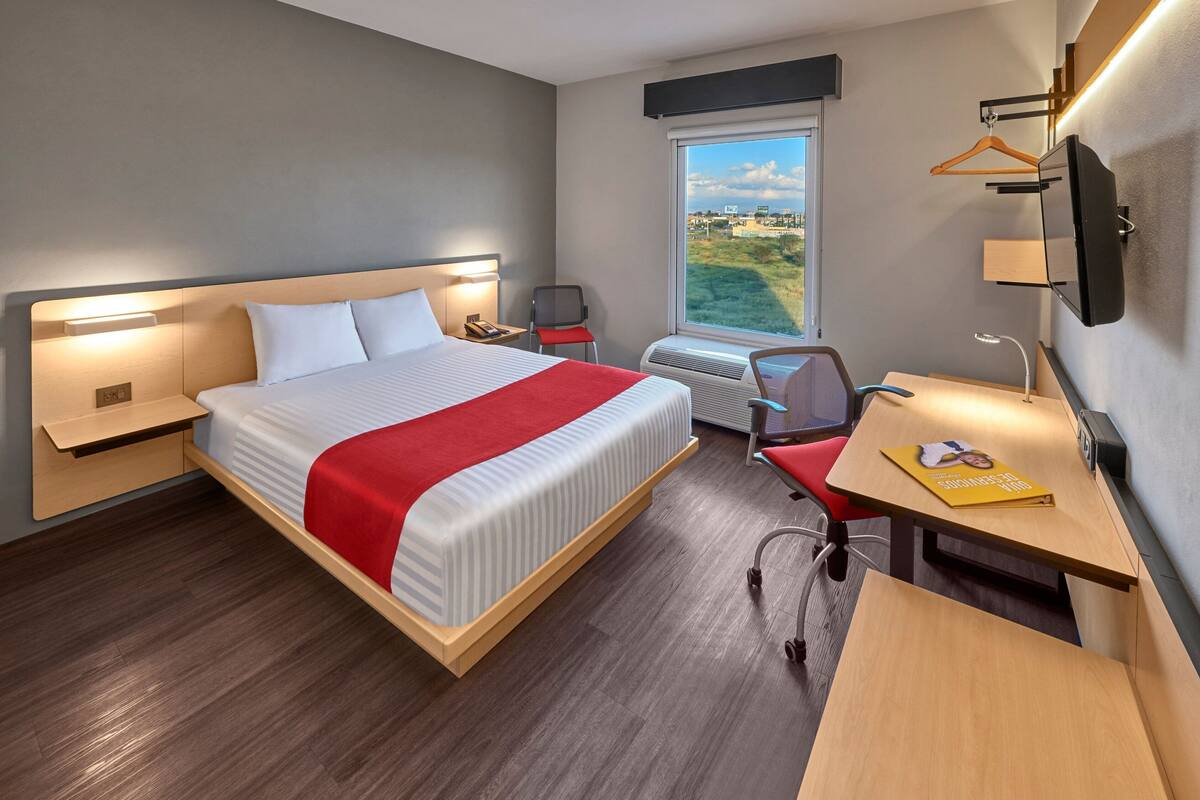 A hotel room with a large bed, a desk, a chair, a TV, and a window with a view.