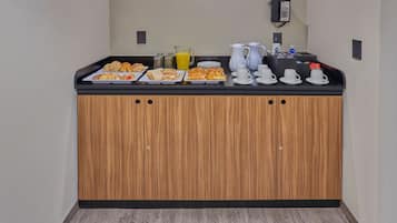 A breakfast buffet with various pastries, a pitcher of orange juice, and coffee cups.