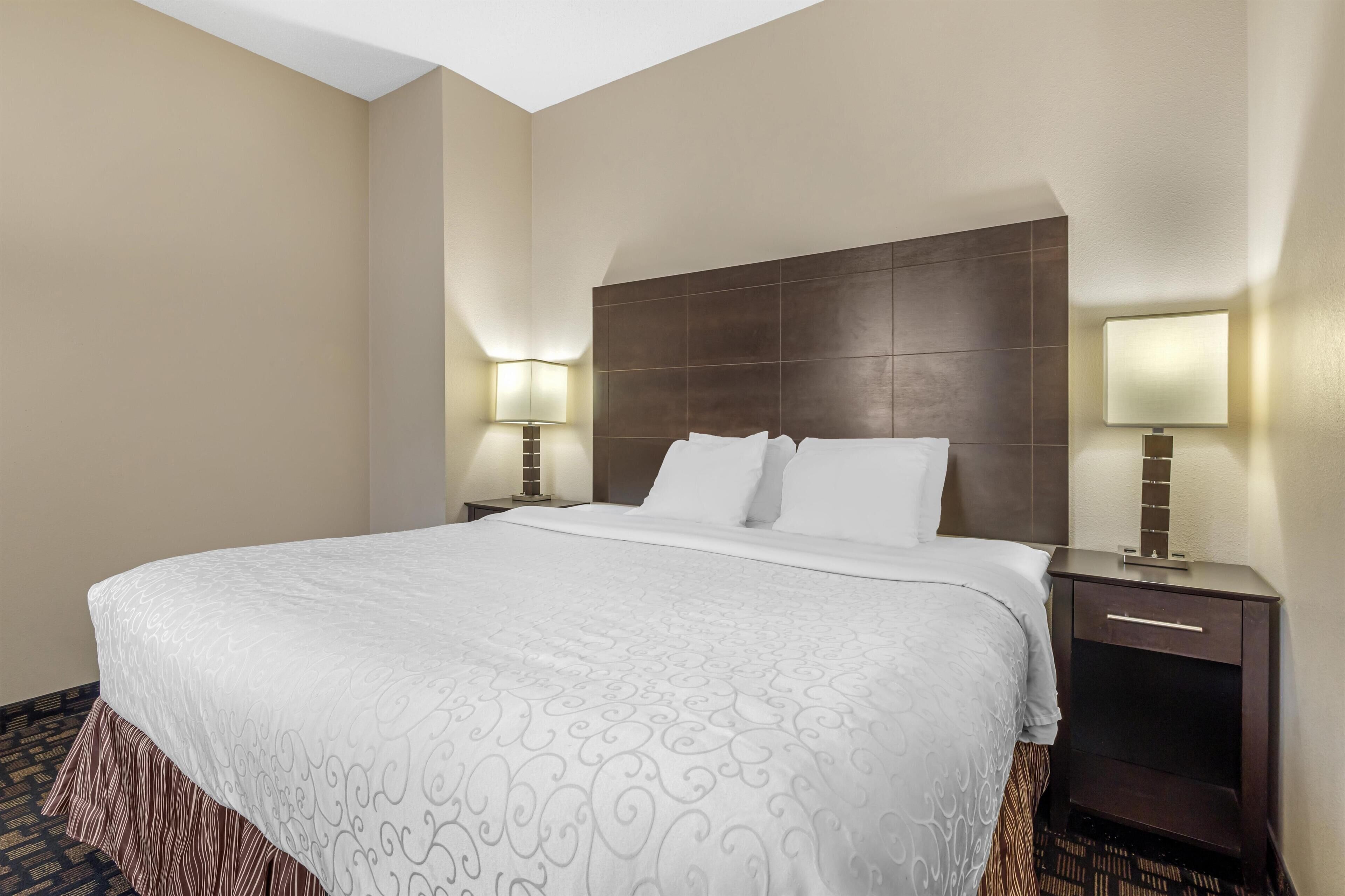 A hotel room with a large bed, two bedside tables with lamps, a dark headboard, and a patterned carpet.