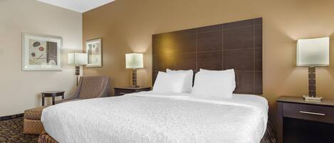 A hotel room with a large bed, a chair, a nightstand, and a lamp.