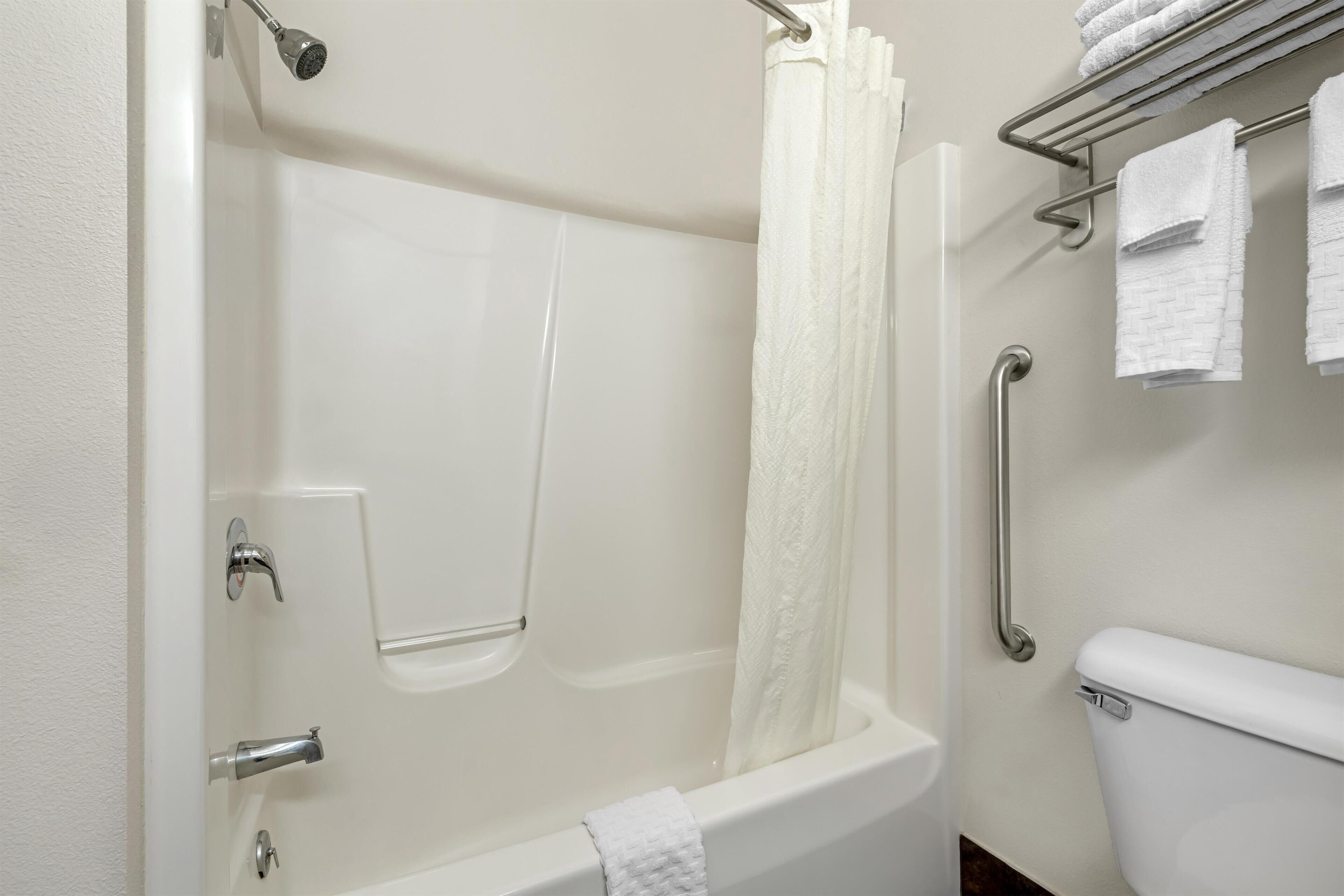 A bathroom with a bathtub, a shower curtain, a toilet, and a towel rack with towels.