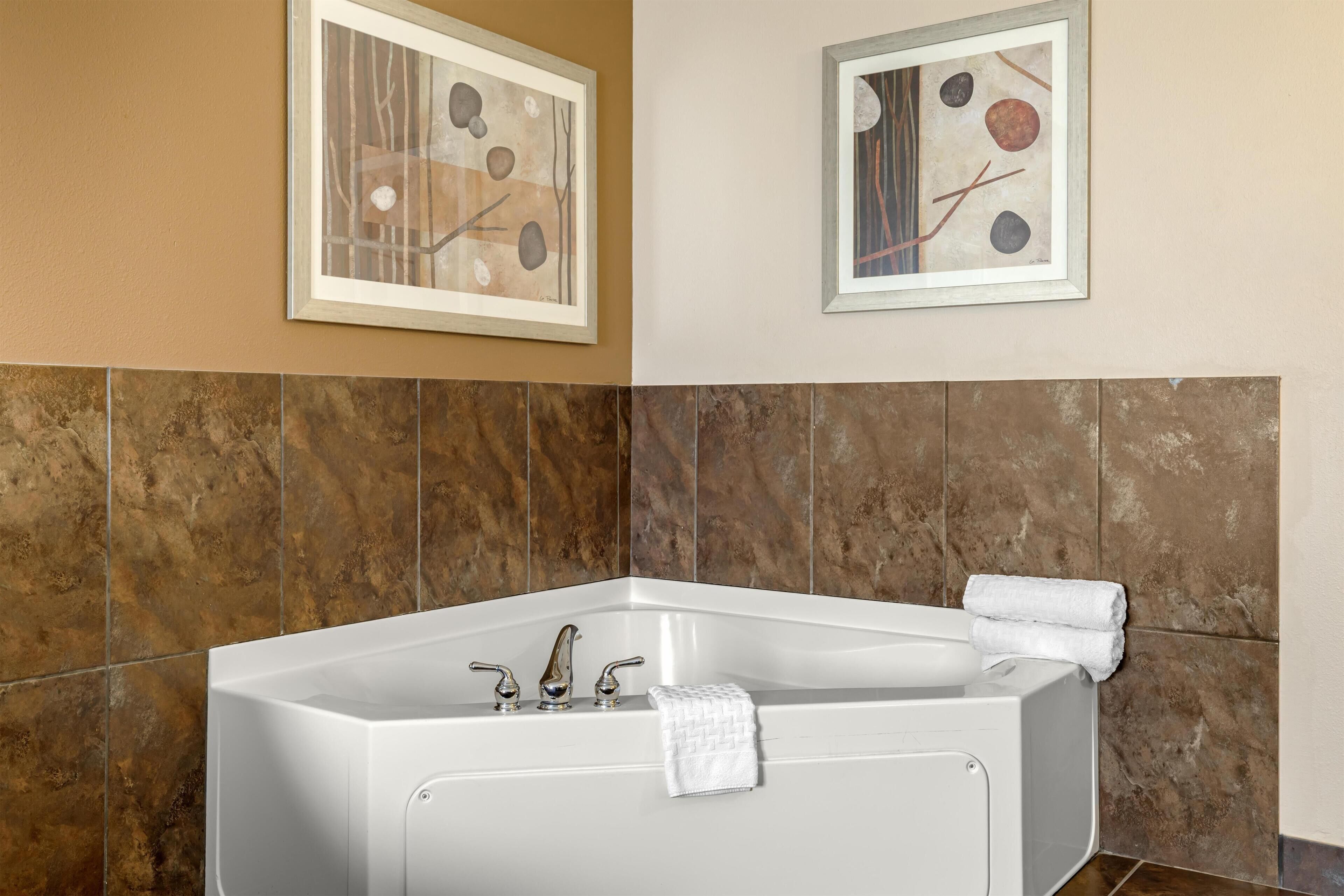 Une salle de bain avec une baignoire sur pieds, deux tableaux abstraits encadrés et un mur recouvert de carreaux.